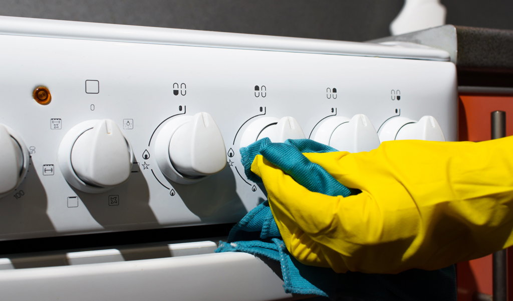 Female hand in glove cleaning panel gas stove with rag, close-up. Hygienic house cleaning.