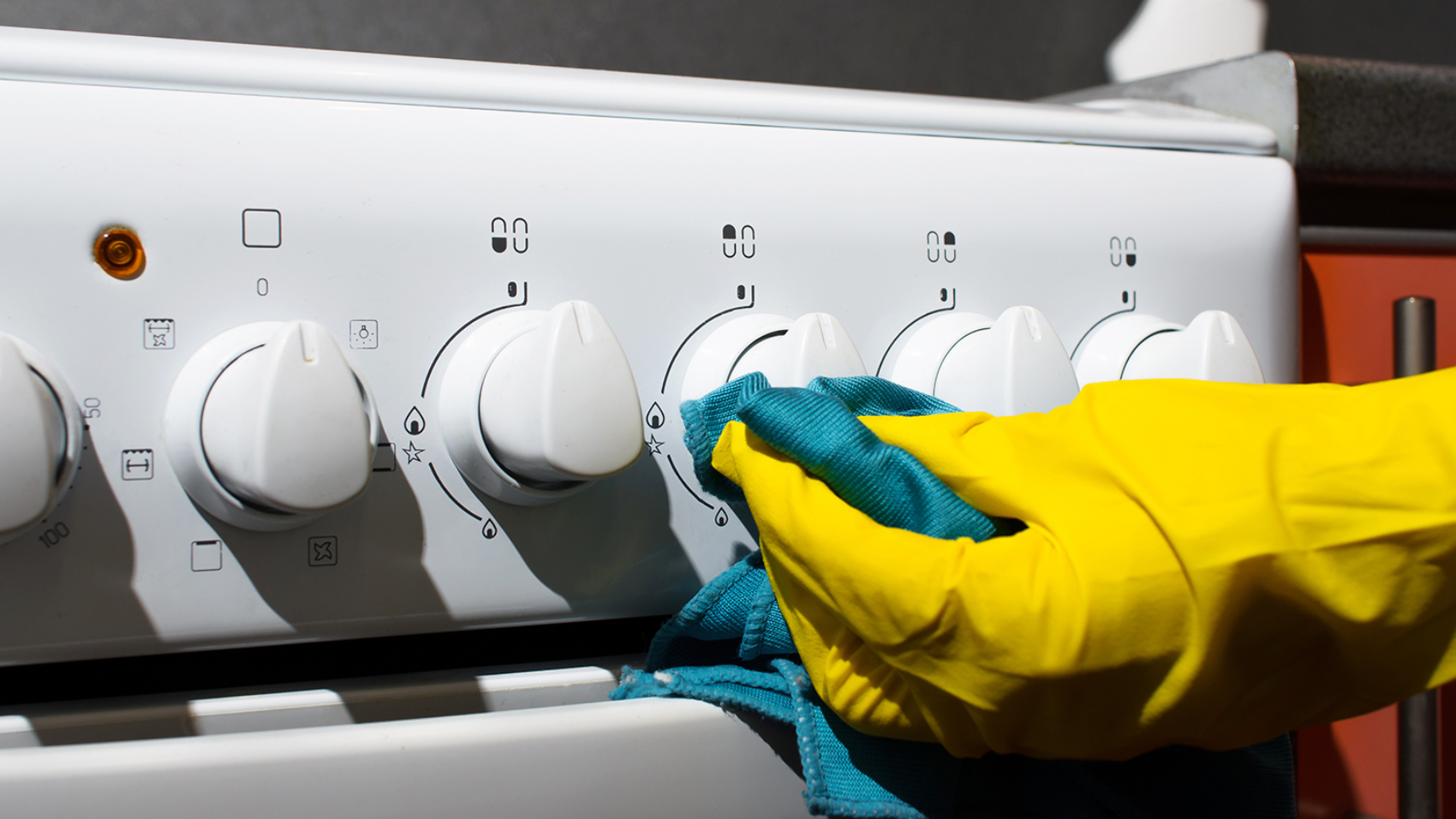 Female hand in glove cleaning panel gas stove with rag, close-up. Hygienic house cleaning.