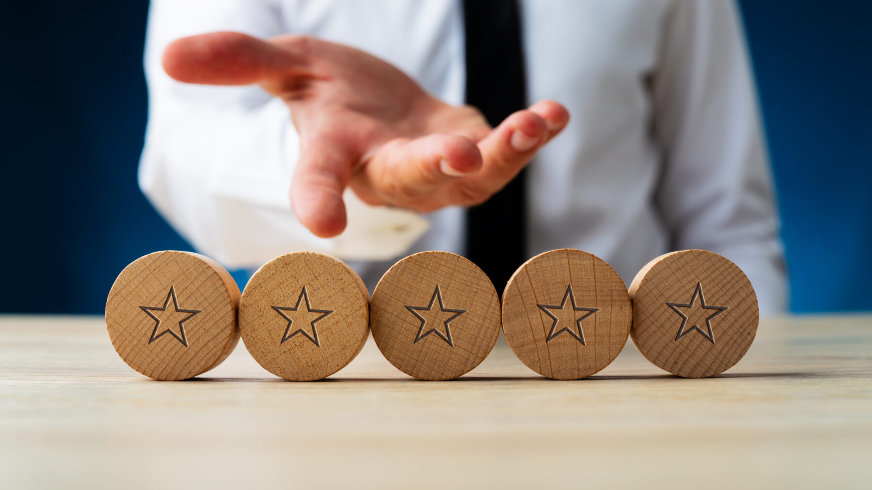 Hand of a businessman presenting five wooden cut circles with stars on them in conceptual image of luxury and wealth.