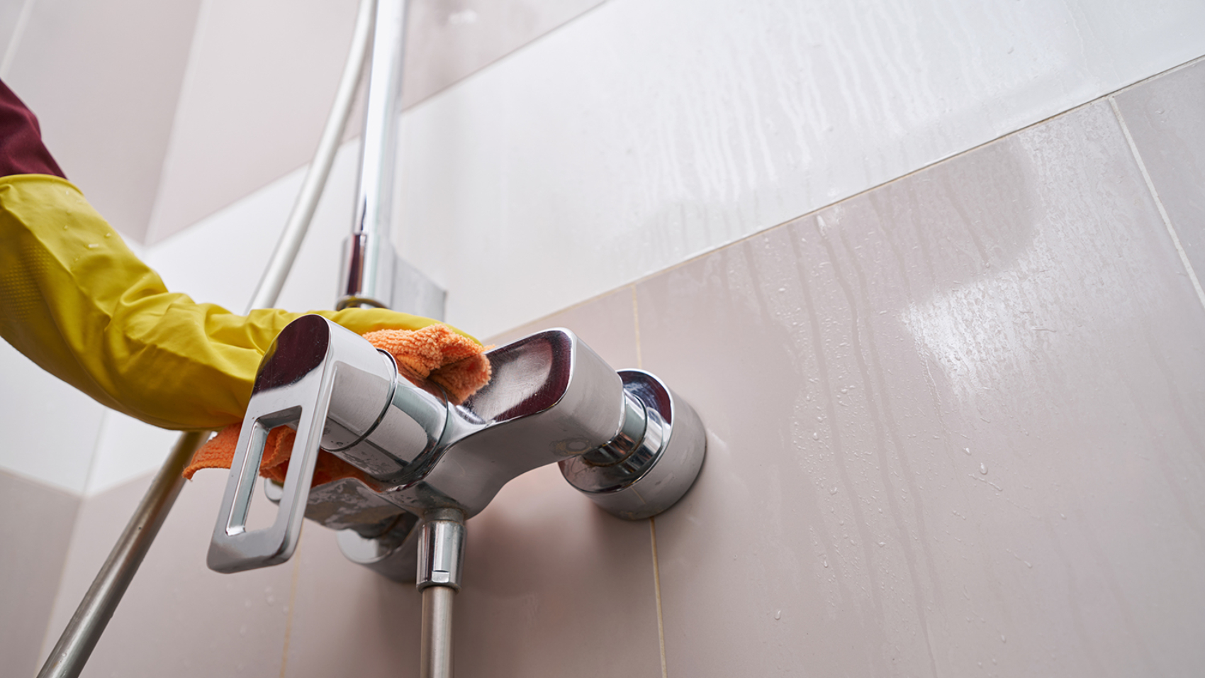 Cropped photo of hand in rubber glove wiping chrome faucet with microfiber cloth