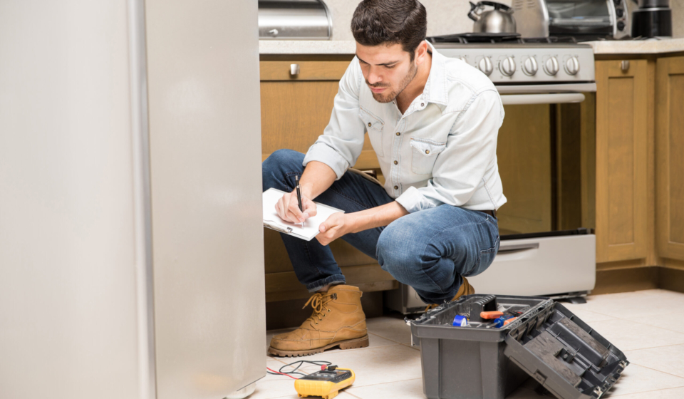 Portrait of a handsome male technician doing a work report on a broken fridge in a home kitchen