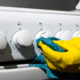 Female hand in glove cleaning panel gas stove with rag, close-up. Hygienic house cleaning.