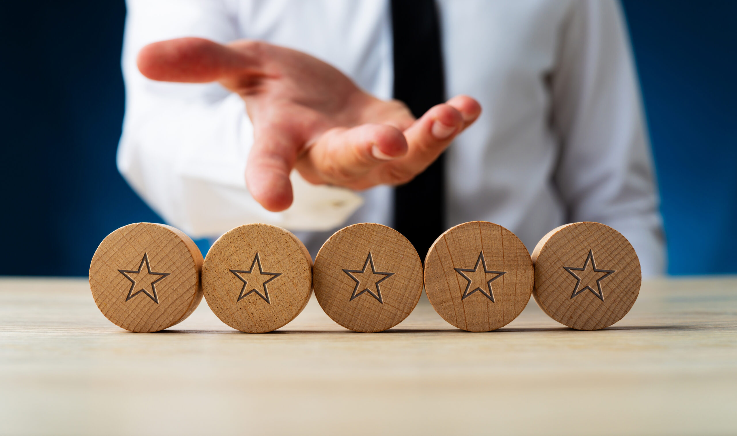 Hand of a businessman presenting five wooden cut circles with stars on them in conceptual image of luxury and wealth.