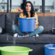 Brunette woman holding bucket on sofa during water damage in living room