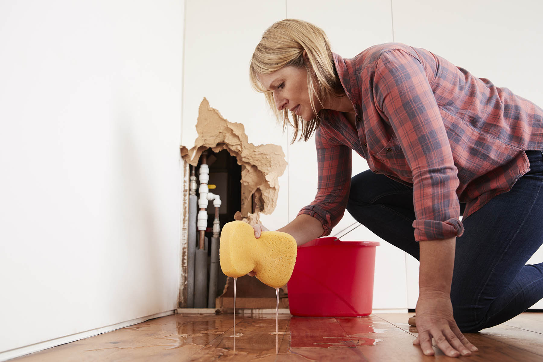 Woman cleaning water damage near a broken wall pipe