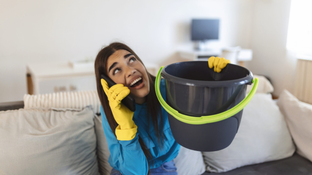 Shocked Woman Calling Plumber While Collecting Water Leaking From Ceiling Using Utensil